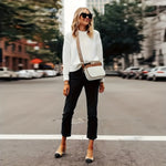 Woman in a white blazer and black pants standing on a city street with vegan leather handbag.